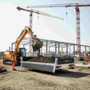Construction site view of an excavator loading a flatbed trailer with dirt, featuring two construction workers.